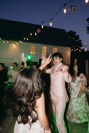 Party guests dance under string lights at an outdoor evening reception with joyful celebration and festive atmosphere.