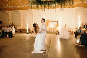Wedding couple sharing first dance in rustic venue with string lights.