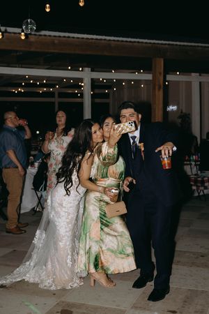 Wedding guests dance and celebrate together at a dimly lit indoor reception venue with string lights overhead.