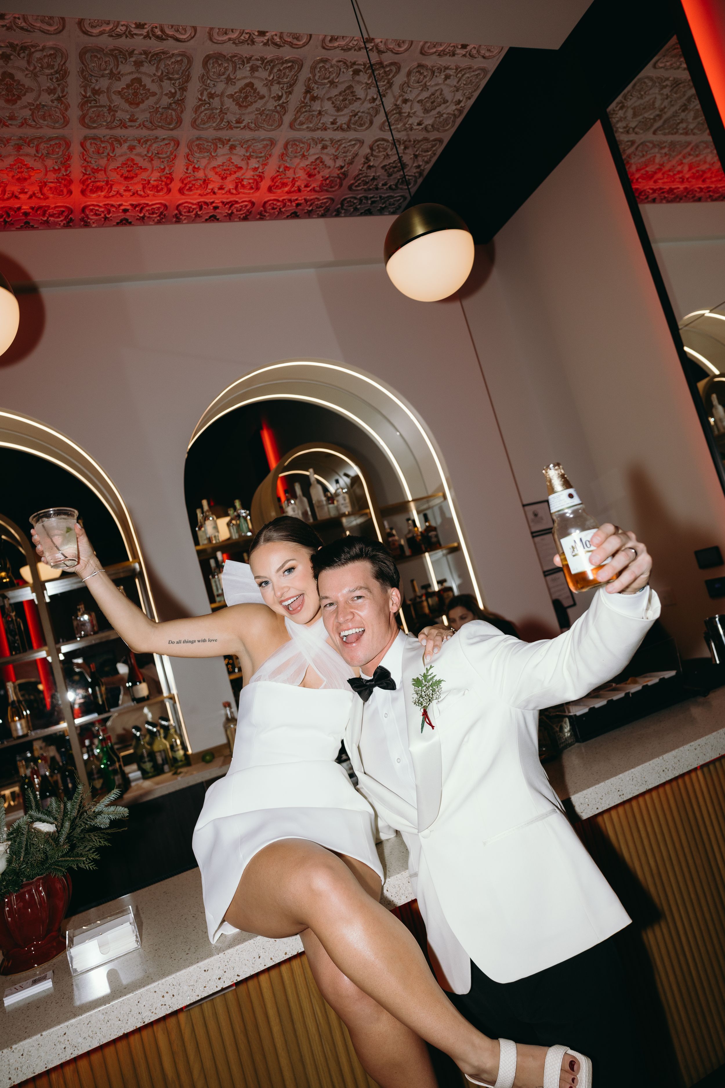 Two people in white outfits dance joyfully at a party venue with decorative ceiling patterns and mood lighting.