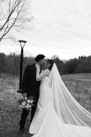 A romantic black and white wedding photo series showing a couple embracing in a field with a flowing long veil.