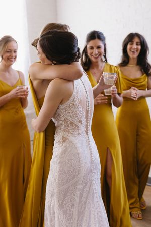 Bridesmaids in mustard yellow dresses stand with bride in white lace gown during wedding celebration.