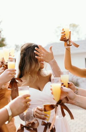 Wedding party toasting with mimosas in white and brown dresses.