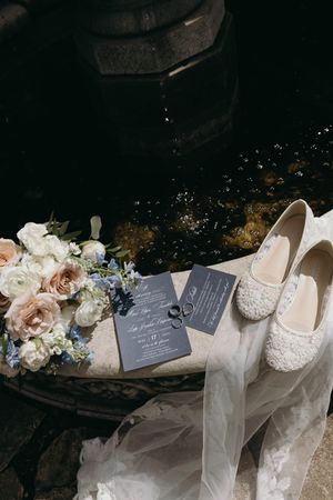 Wedding details including elegant lace shoes, delicate floral arrangements, and handwritten invitation cards laid out on dark surface.