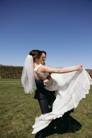 A couple embraces in a joyful dancing pose on a grassy field under bright blue sky.