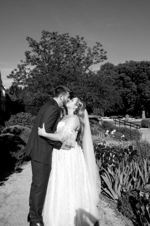 A black and white wedding portrait of a couple sharing an intimate moment in a garden path.