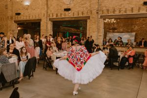 A dancer in a white tulle skirt and red top twirls on the dance floor at a wedding reception.