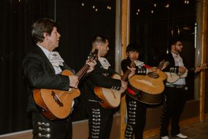 Mariachi band performing with guitars in traditional outfits against a dark background.