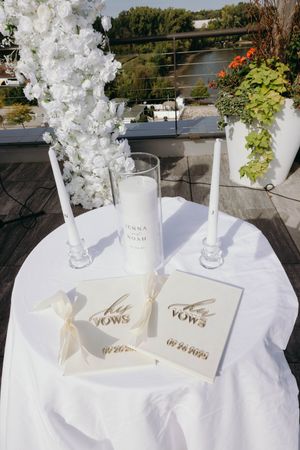 Elegant white floral arrangements with 'vows' signage displayed on crisp white tablecloths for a wedding ceremony setup.