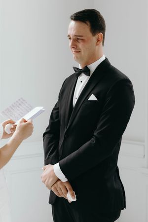 A person in a black tuxedo and bow tie holds papers while standing against a white background in a series of poses.