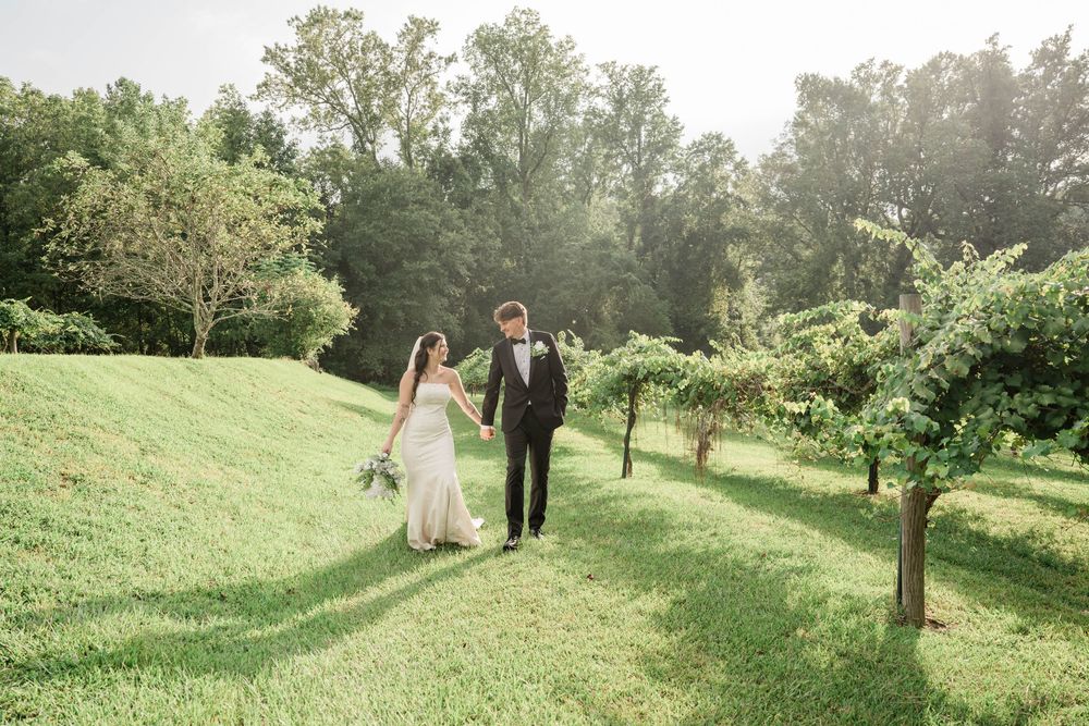 Wedding couple walking through sunlit garden pathway with lush greenery.