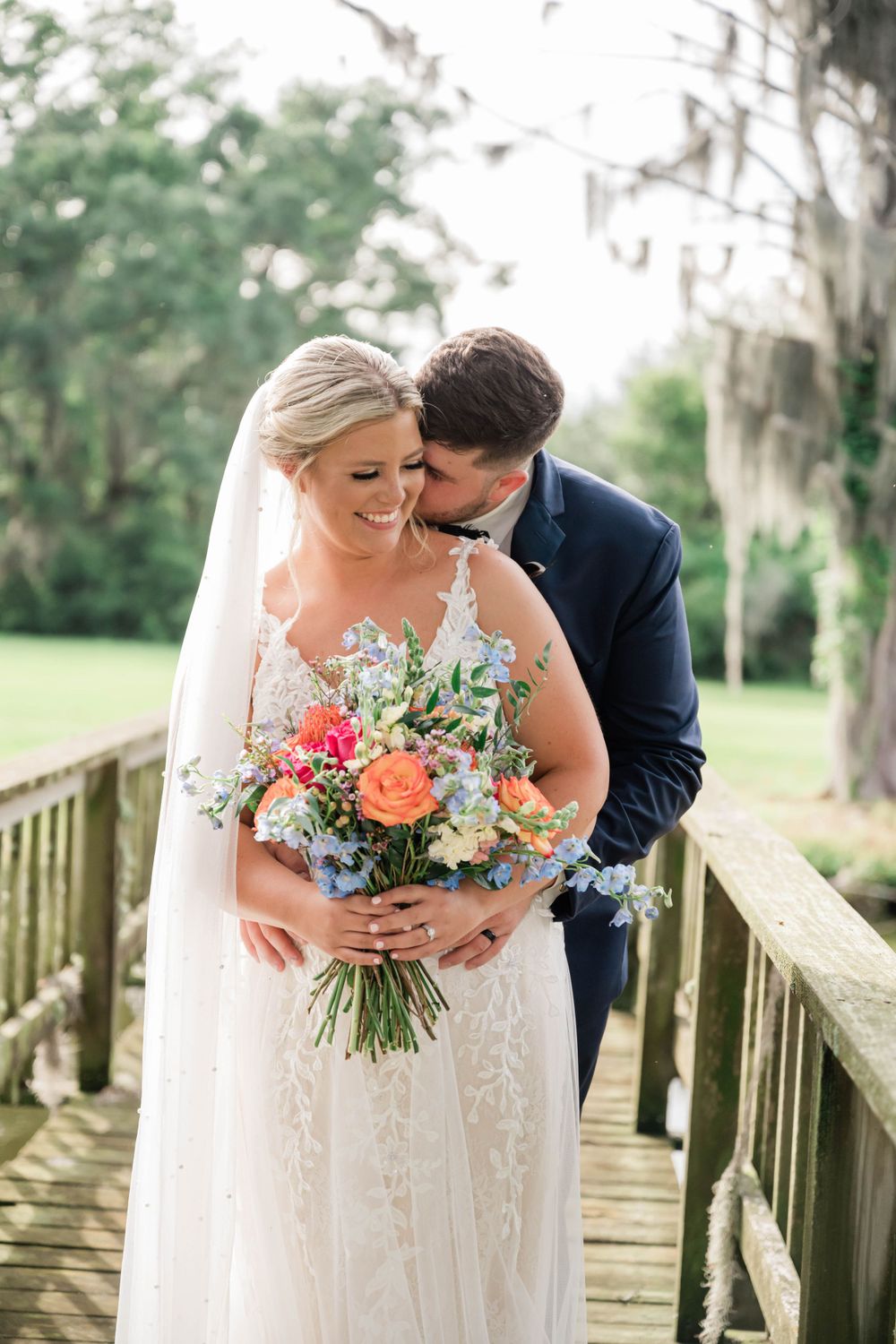 Romantic couple shares tender moment on wooden boardwalk with floral bouquet.