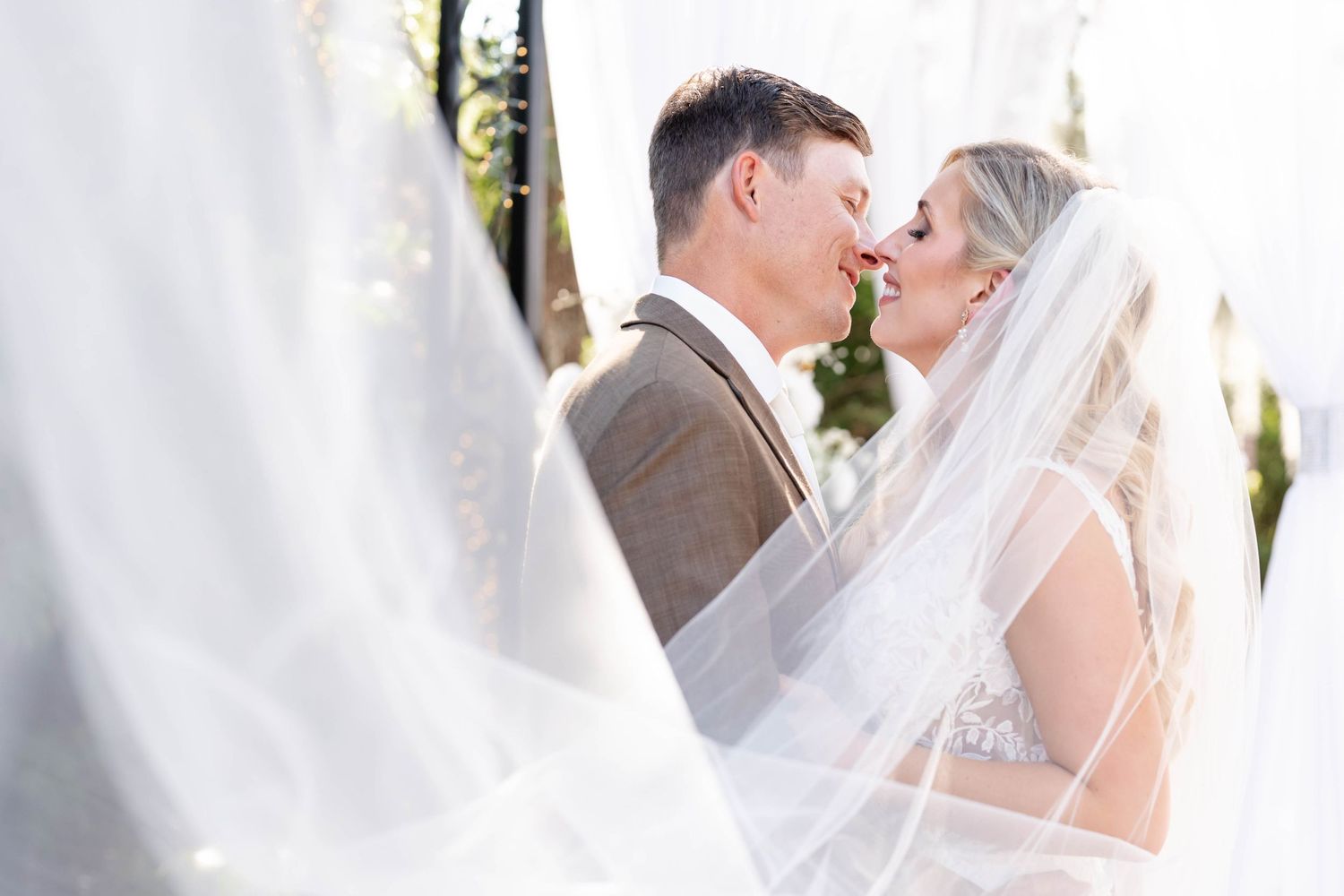 Wedding couple sharing an intimate moment behind a flowing white veil.