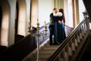 Couple embracing on elegant staircase with silver candelabra in foreground at romantic venue.