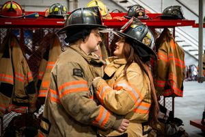 Couple in firefighter gear sharing a romantic moment in a fire station gear room.