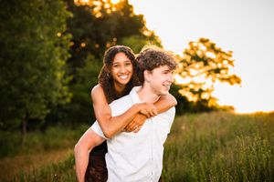 A young couple shares a joyful piggyback ride in a sunny green field at golden hour.