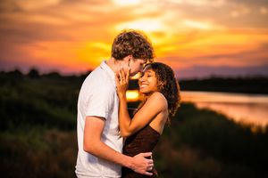 Romantic couple sharing a tender moment at sunset with vibrant orange sky and serene lake backdrop.