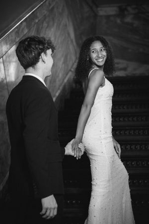 Black and white wedding photo of a bride in a white gown smiling at her groom on an elegant staircase.