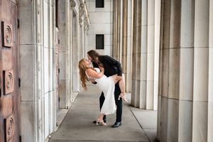 Couple sharing a romantic dip kiss between stone columns at an elegant outdoor venue.