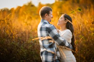 A couple embraces and smiles at each other in a golden autumn field during a romantic outdoor engagement photo session.