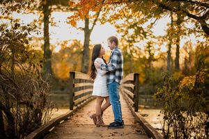 Couple embracing on a wooden bridge surrounded by colorful autumn foliage in a romantic fall engagement photo.