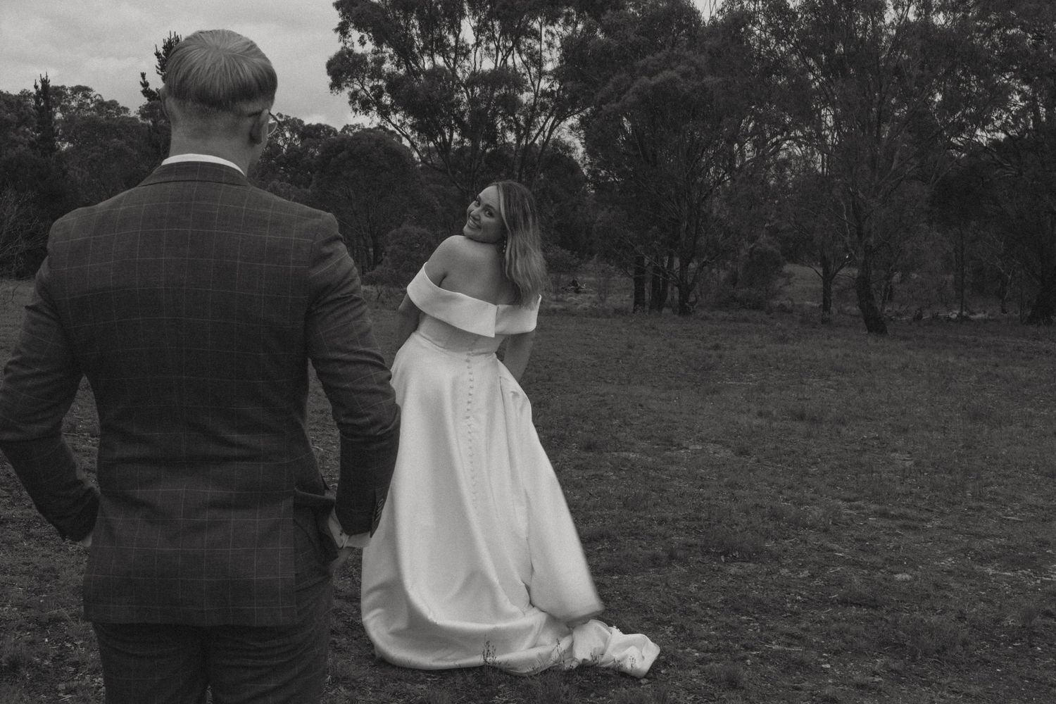Husband looking lovingly at his wife whilst she looks over her shoulder at the camera on her wedding day.