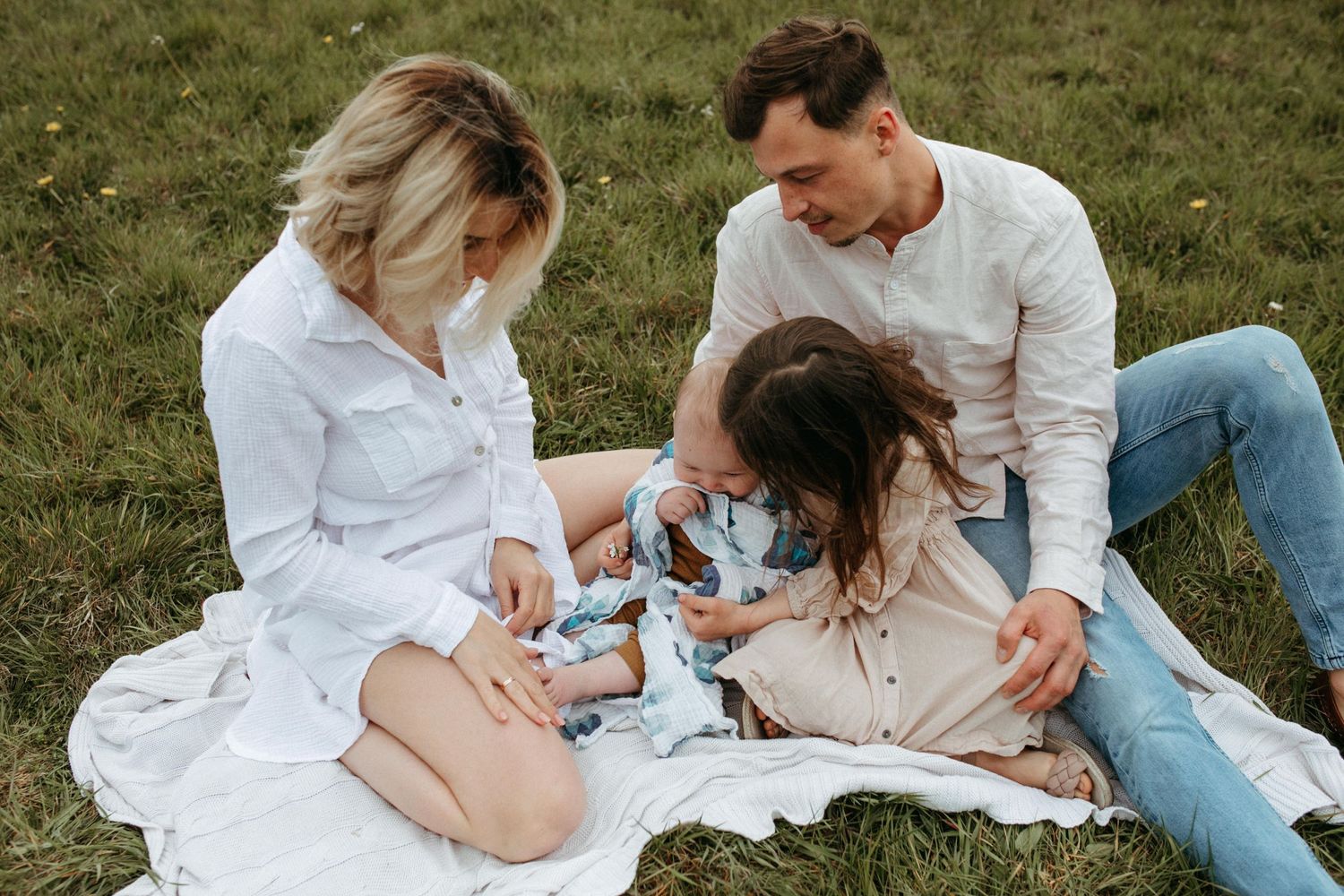 Couple having a picnic on a white blanket in a grassy field on a cloudy day.
