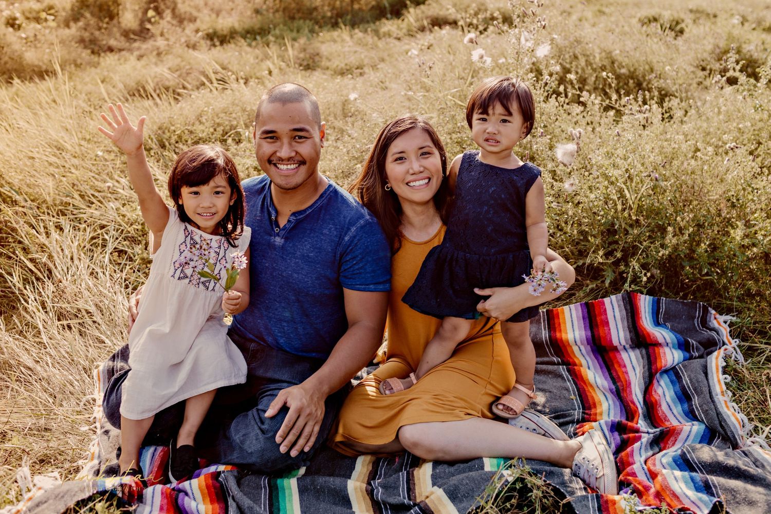 Family sitting on striped blanket during golden hour outdoor photo session.