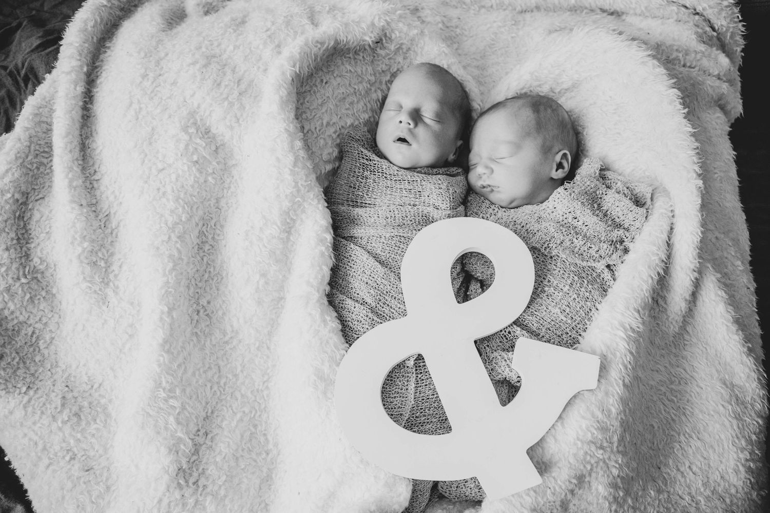 a black and white photo of twin girls wrapped up in a blanket shaped like a heart with an & sign laid on them