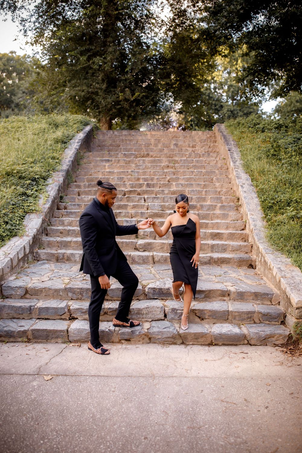 A playful moment captured on stone steps as couple in black formal wear dance together.