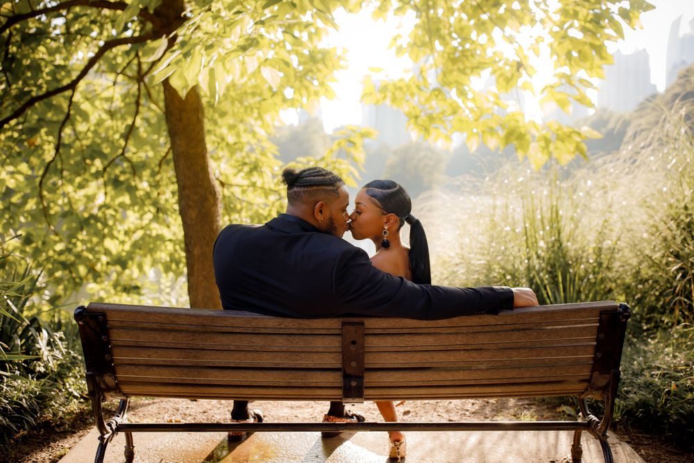A couple shares a romantic moment on a park bench at sunset with golden light filtering through trees.