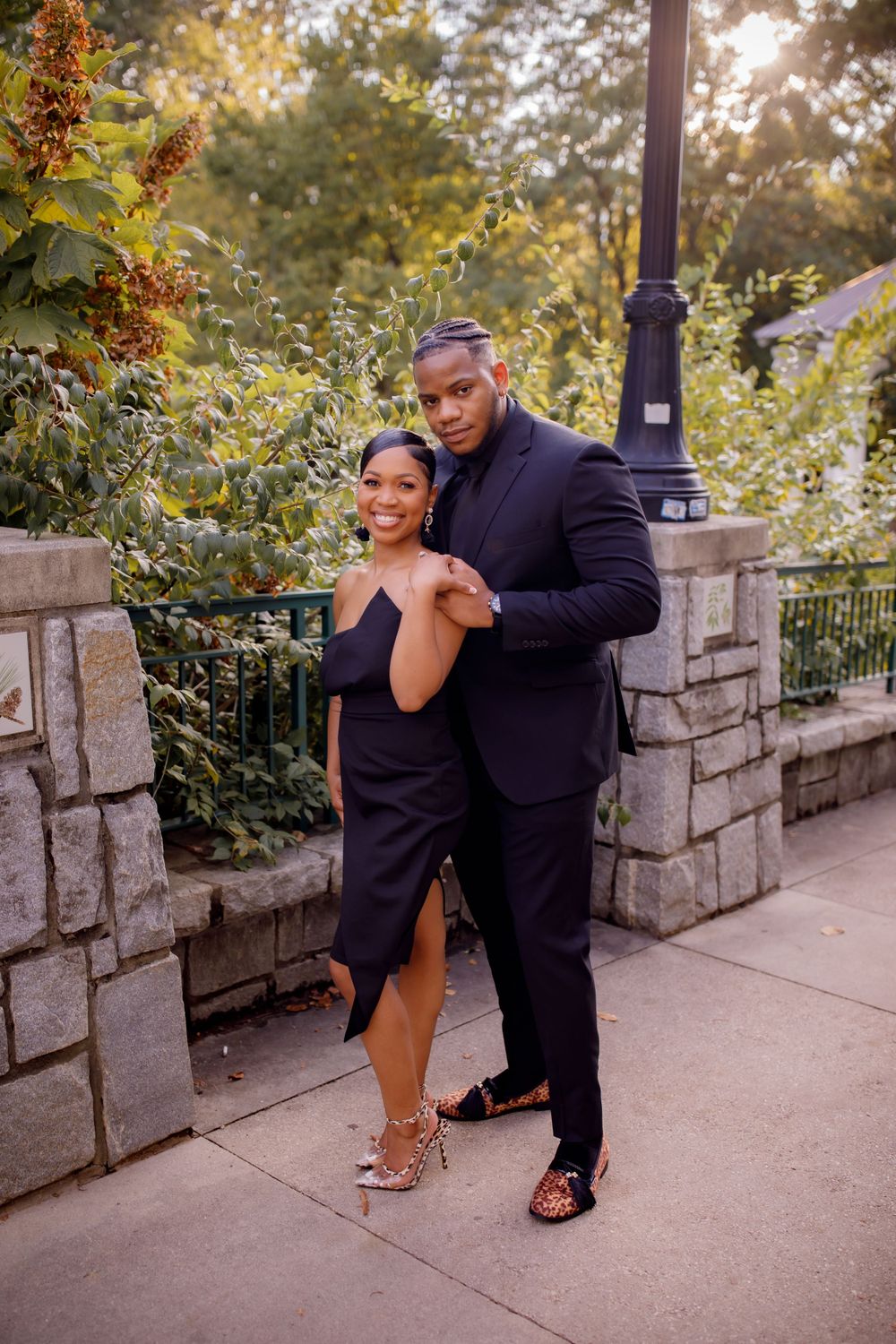 A couple poses elegantly against a stone wall backdrop in coordinated evening wear.