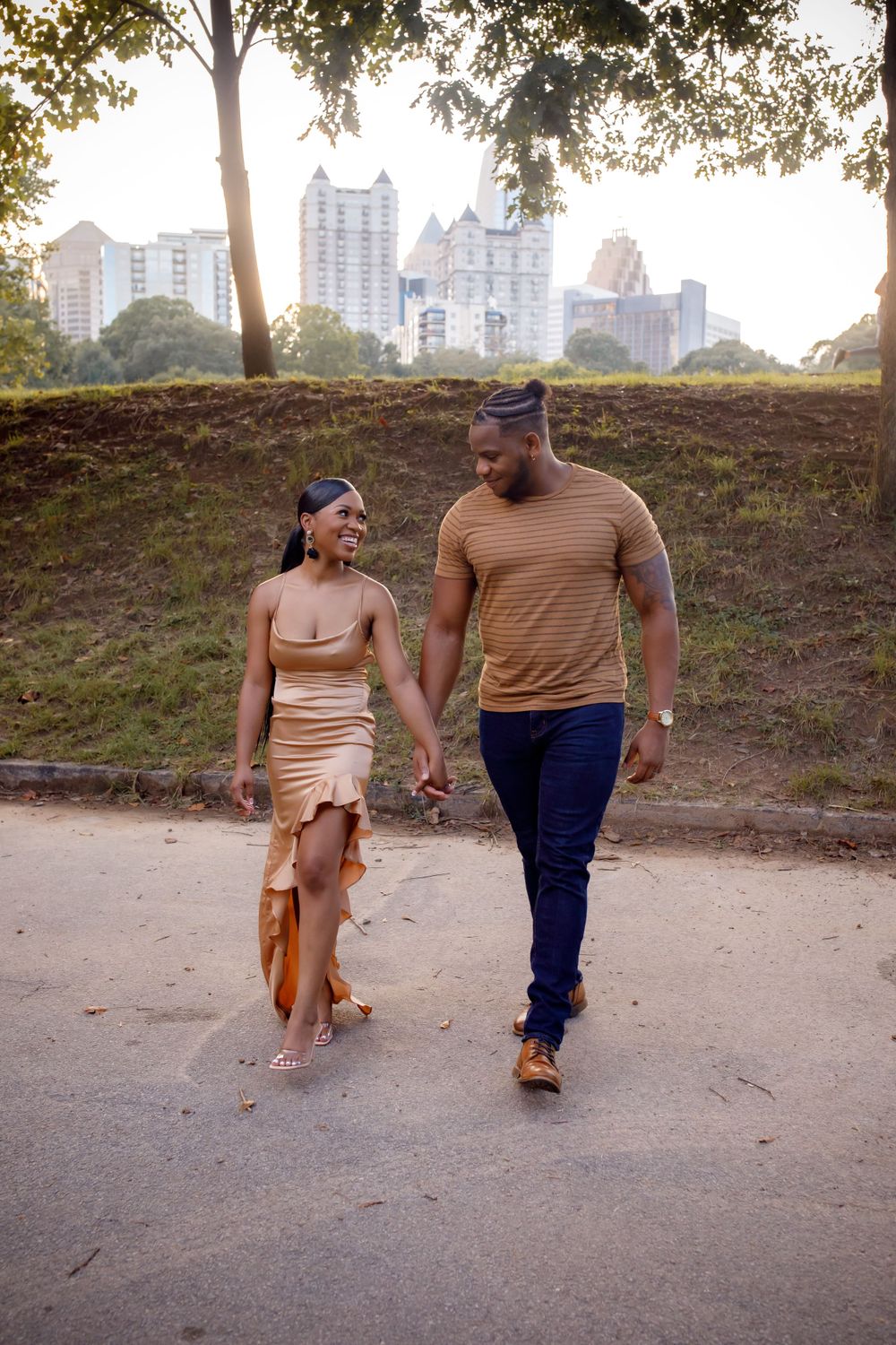 A couple takes a romantic walk along a path with the Atlanta cityscape in the background.