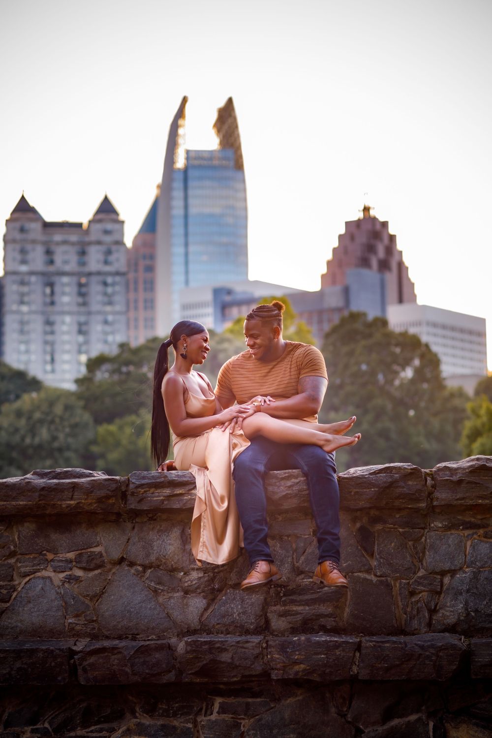 A couple sits together on stone wall enjoying conversation with Atlanta skyline visible behind them.