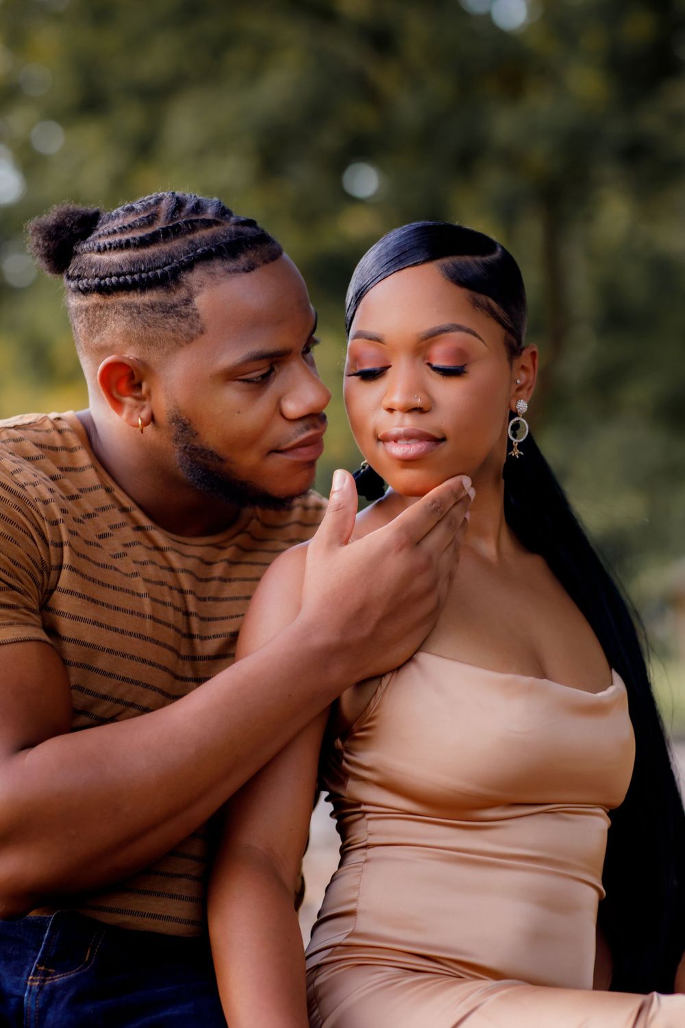 Intimate couple poses outdoors in natural lighting with one wearing a striped shirt and the other in a beige dress.