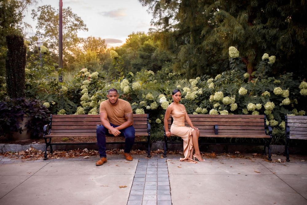 Couple sitting apart on park bench surrounded by white hydrangea bushes at sunset.