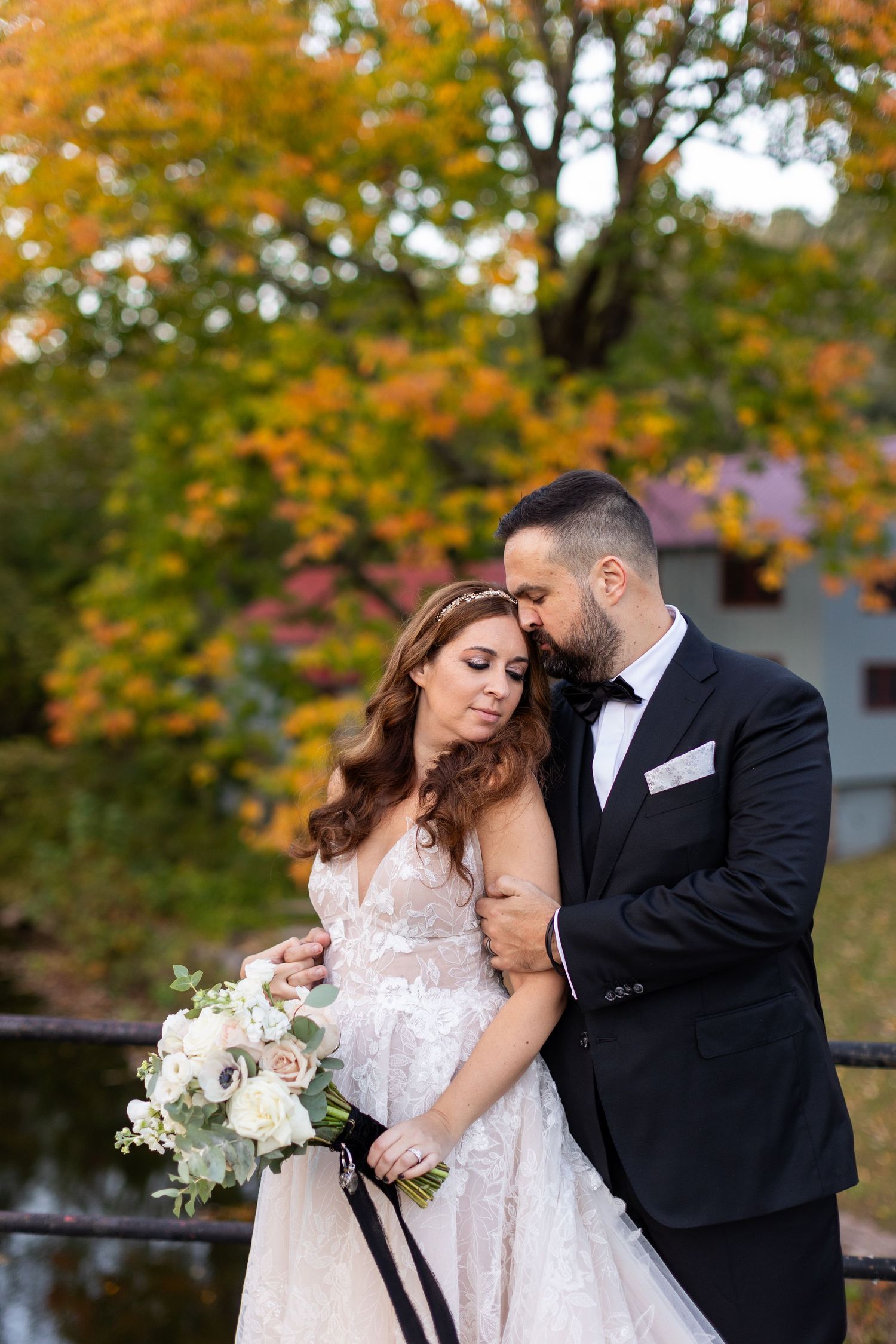 Beautiful autumn wedding portrait with fall foliage and white bouquet by a pond.