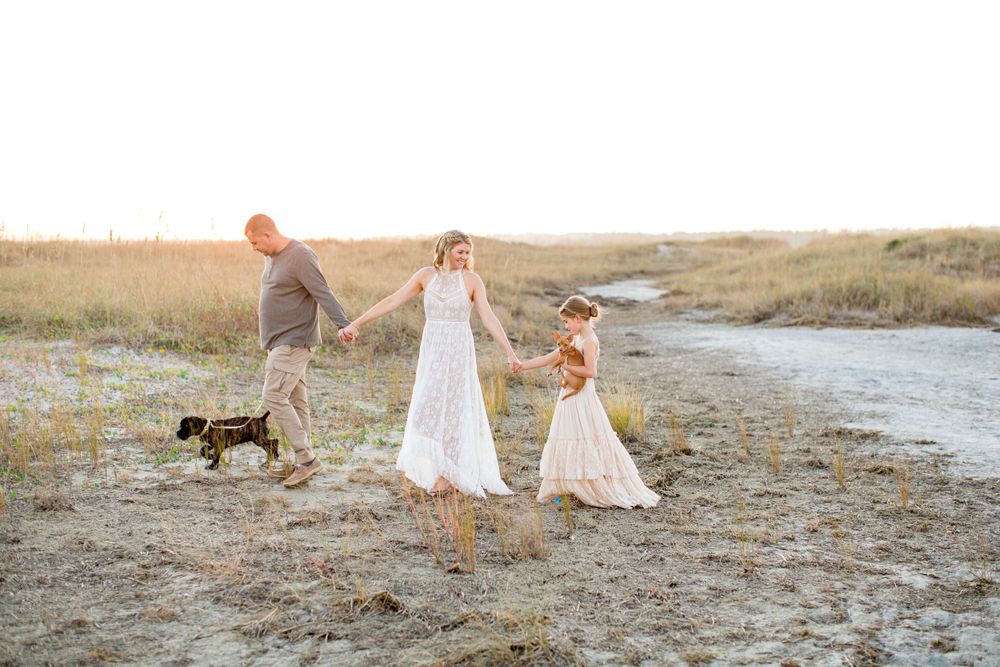 Family walking on beach path with their dog during golden hour.