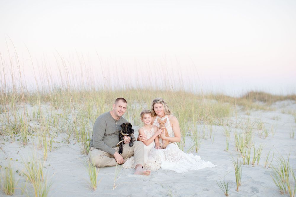Family sitting on beach dunes with their dog during sunset.