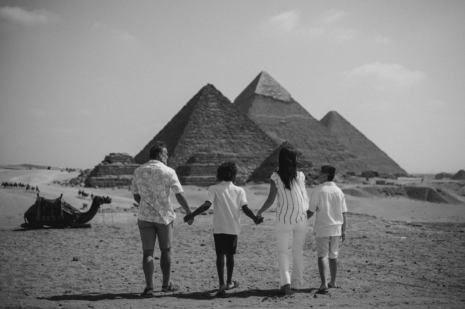 Silhouettes of people holding hands while facing the pyramids of Giza in black and white.