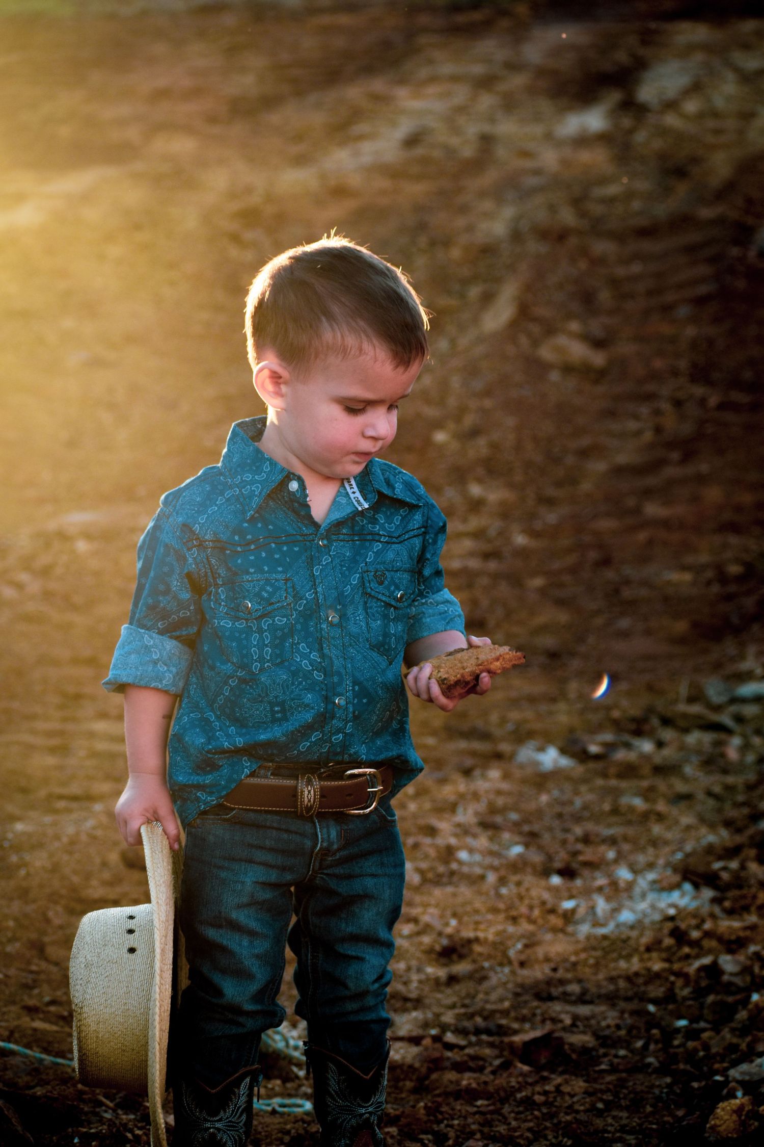 Young child in blue shirt plays outdoors during golden hour sunset creating warm nostalgic mood.
