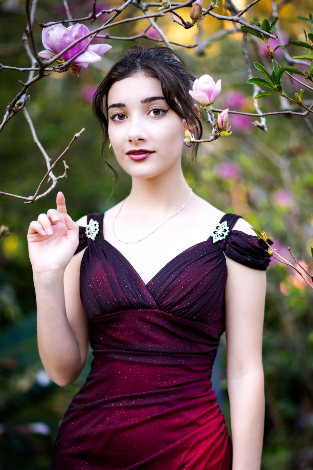 Classic burgundy evening dress with delicate floral accents against blooming magnolia branches.