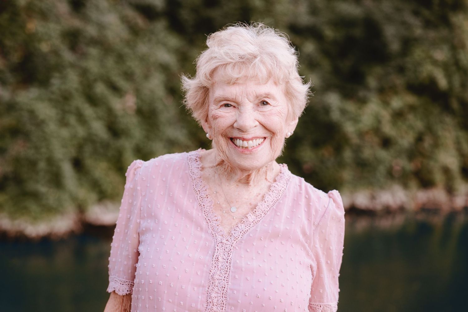 Closeup portrait of senior woman in pink top smiling brightly outdoors.