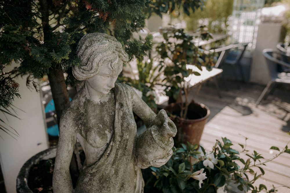 Classical stone garden statue nestled among green foliage in an outdoor setting.