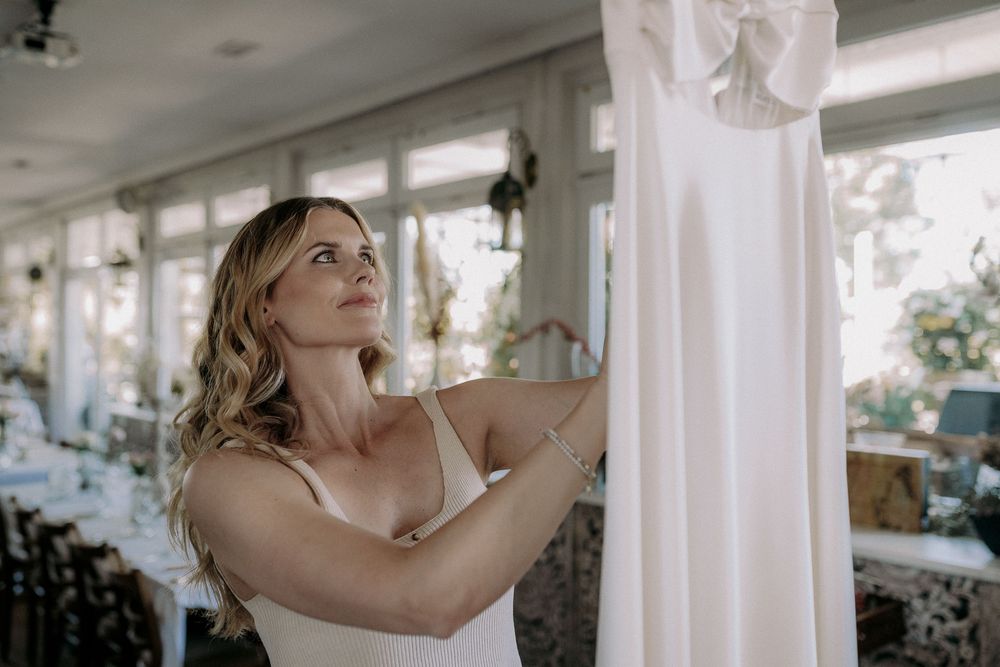 Woman in bridal gown examining white dress details.
