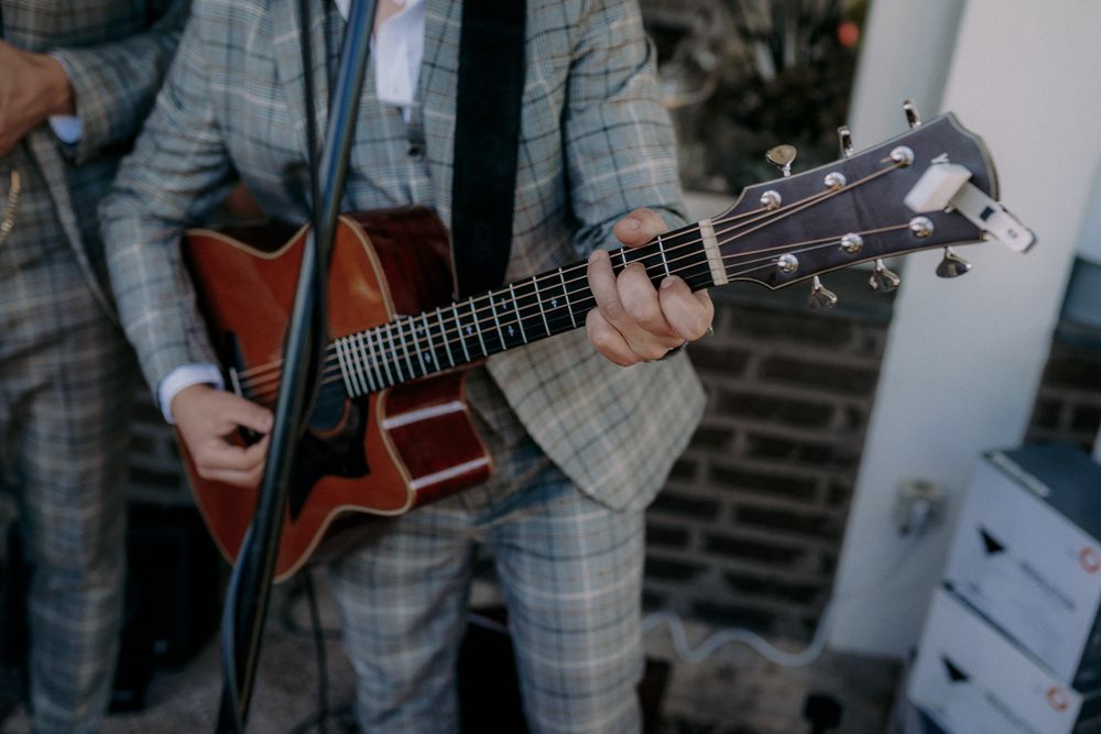 Musician in plaid suit playing acoustic guitar at outdoor event.