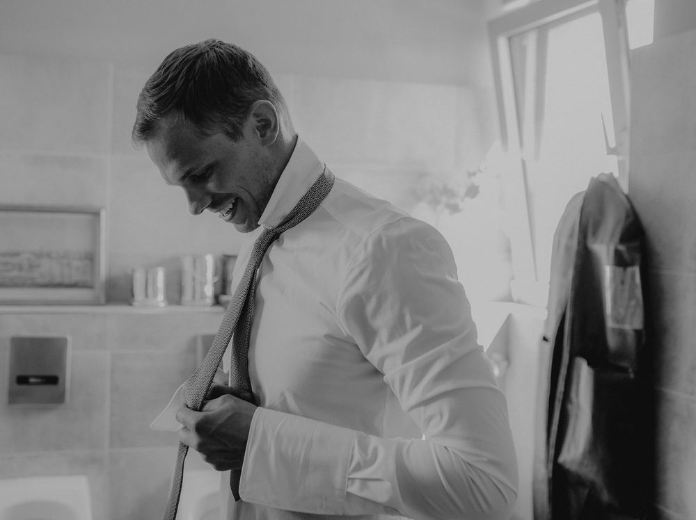 Person adjusting tie in black and white photo while getting dressed.