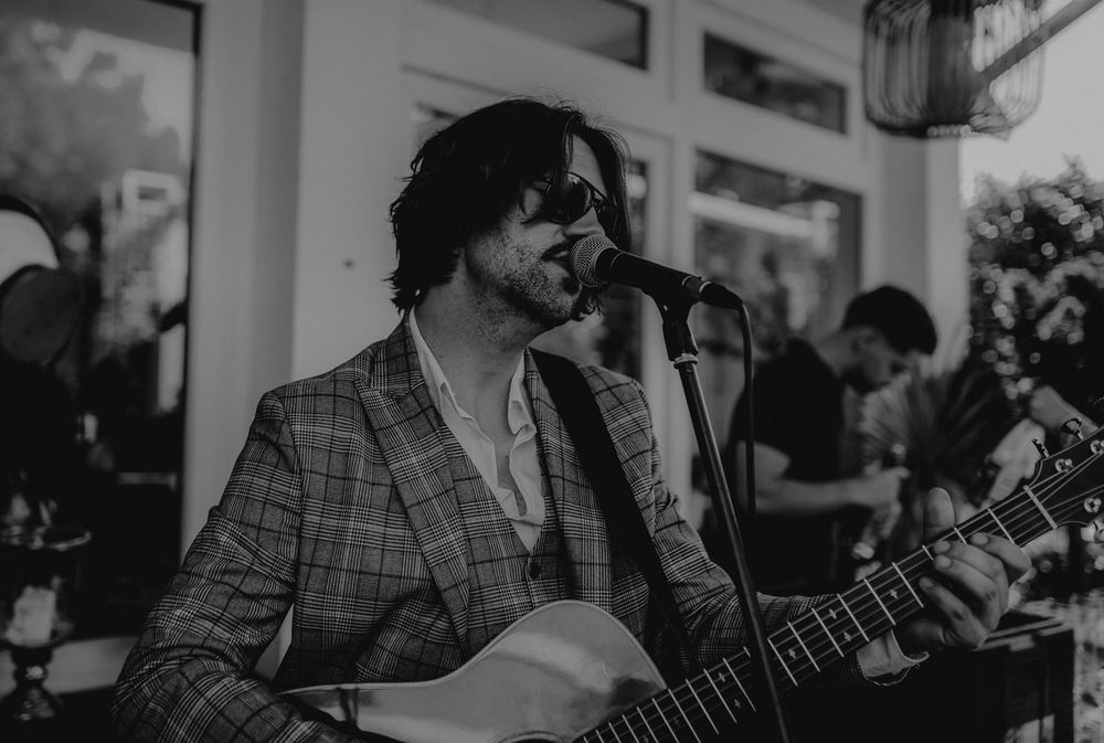 Black and white photo of musician performing with guitar at indoor venue.