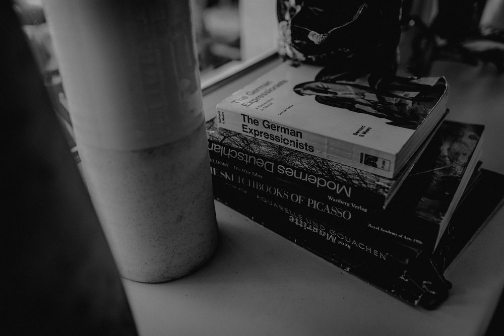 A stack of books with a white container on top photographed in moody black and white lighting.
