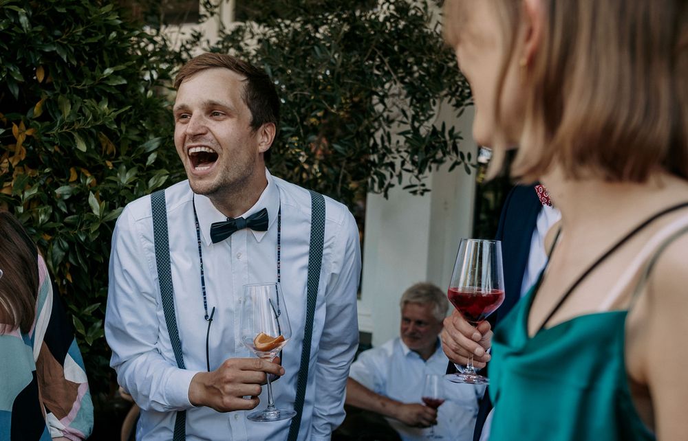A person in a bowtie and suspenders laughing during a lively outdoor celebration.